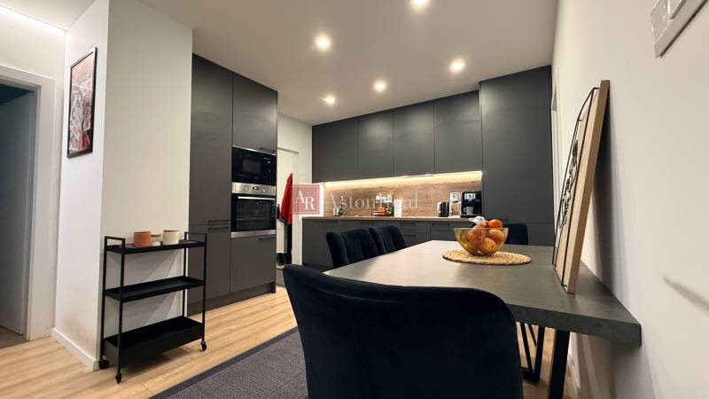 Küche in einer 4-Zimmer-Wohnung mit Holzboden, schwarzen Schränken und Esstisch.