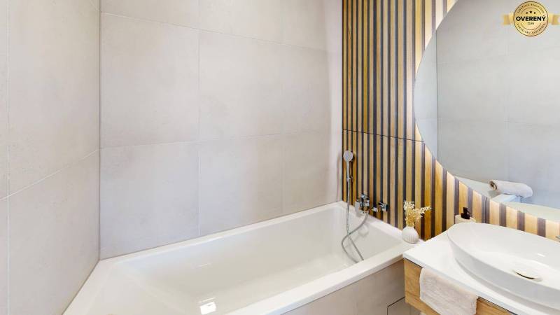 Badezimmer mit Badewanne, Waschbecken und dekorativer Holzverkleidung an der Wand.