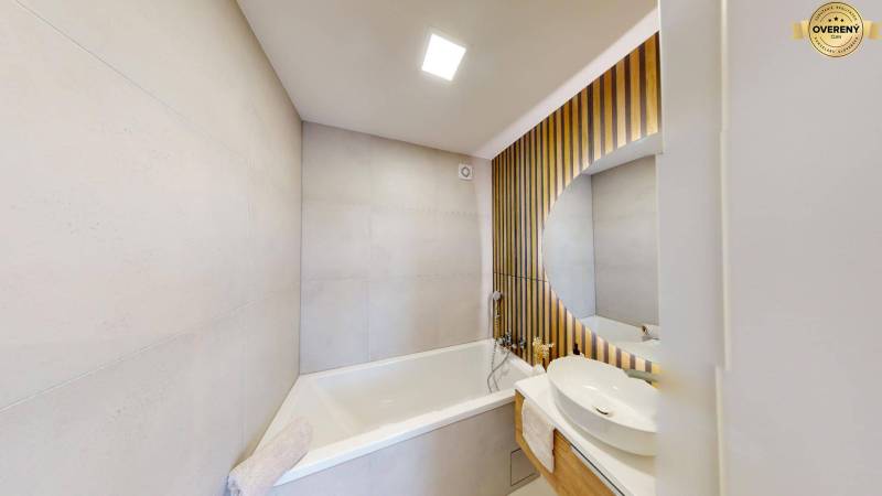Badezimmer mit Badewanne und Waschbecken, Holzverkleidung an der Wand.