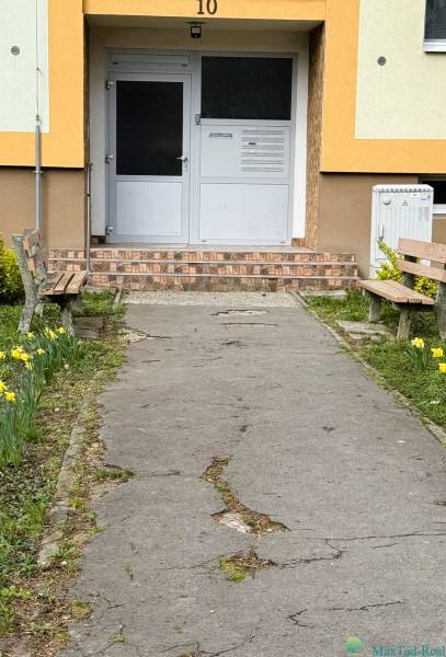 Eingang zum Gebäude in der Škultétyho-Straße in Trebišov mit Bänken und Blumenbeeten.