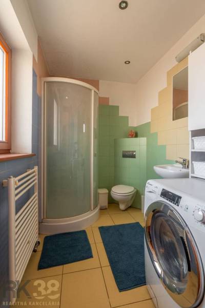 Badezimmer in einem Einfamilienhaus mit Waschmaschine, Duschkabine und bunten Fliesen.