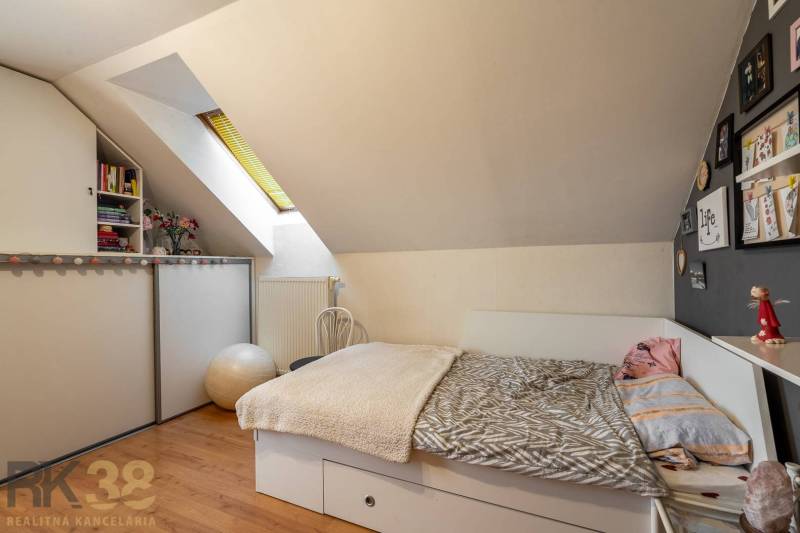 Dachzimmer mit Bett, Regalen, Dekorationen und Holzboden in einem Einfamilienhaus.