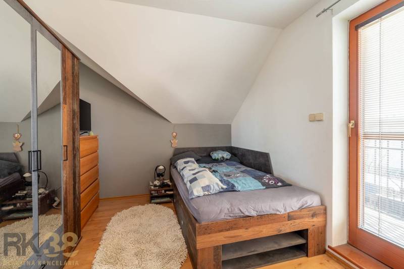 Ein Schlafzimmer in einem Einfamilienhaus mit einem gemütlichen Bett, einer schrägen Decke und einem Boden in Holzoptik.