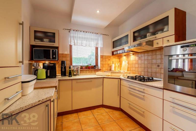 Eine Küche in einem Einfamilienhaus mit eingebauten Geräten, einer Keramikspüle und einem Fenster.