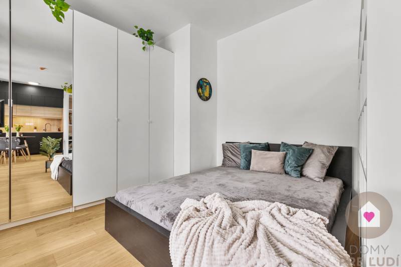 Schlafzimmer in einer Einzimmerwohnung mit Bett, weißem Schrank und Holzboden.