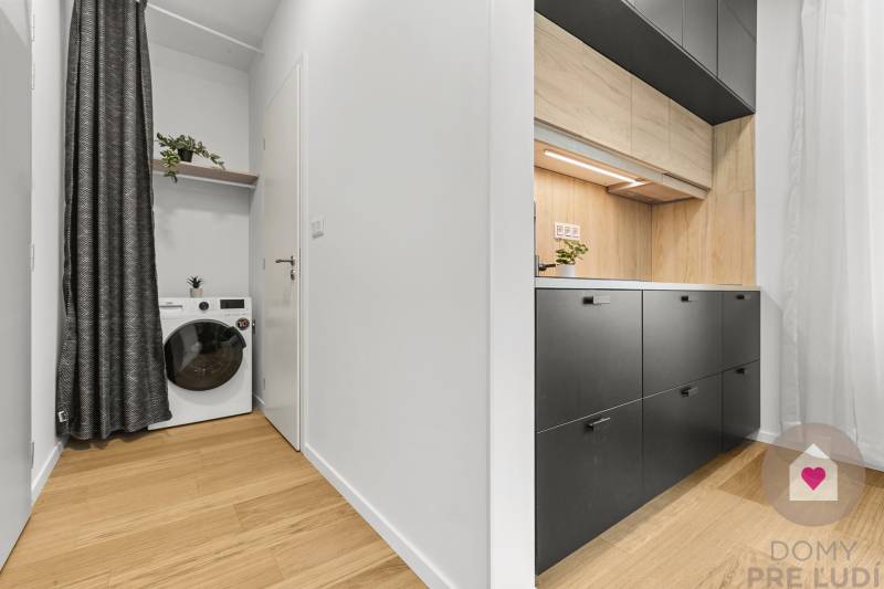 Küche in einer Einzimmerwohnung mit Holzboden und einer Waschmaschine mit Regal.