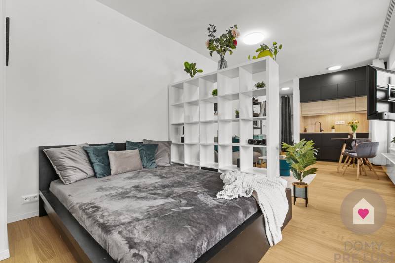 Einzimmerwohnung mit Bett, Regal, Holzboden und schwarzer Küche.