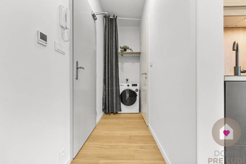 Ein enger Flur in einer Einzimmerwohnung mit einem Vorhang und einer Waschmaschine.