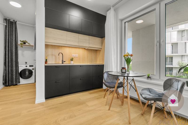 Küche in einer Einzimmerwohnung mit schwarzen Möbeln, Waschmaschine und Holzboden.