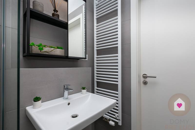 Badezimmer in einer Einzimmerwohnung mit Waschbecken, Handtuchheizkörper und Ablagefächern.