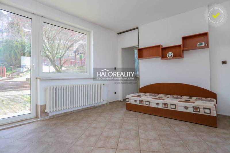 Innenraum eines Einfamilienhauses mit Bett, Regalen, Heizkörper und großem Fenster.