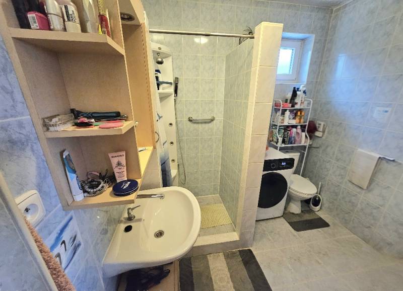 Badezimmer in einem Einfamilienhaus mit Waschbecken, Dusche, Waschmaschine und offenem Regal mit Kosmetik.