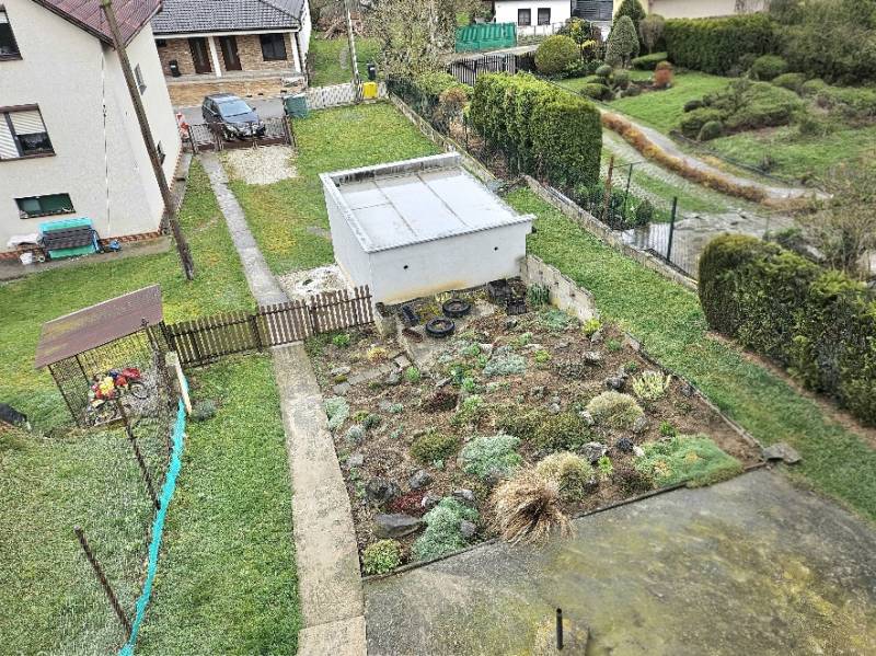 Ein Einfamilienhaus in Horné Ozorovce, Bánovce nad Bebravou, zeigt einen Garten mit einem Blumenbeet und einer Garage.