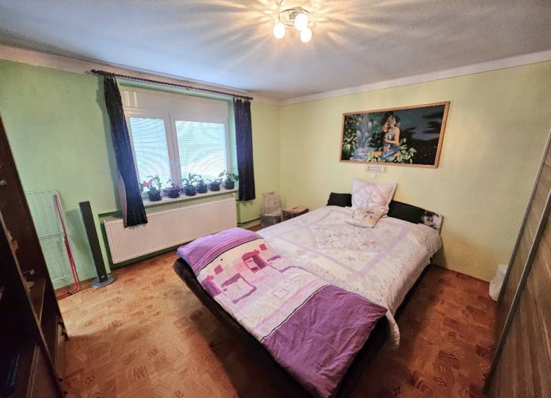 Ein Schlafzimmer in einem Einfamilienhaus mit einem Bett, grünen Wänden und einem Boden in Holzoptik.