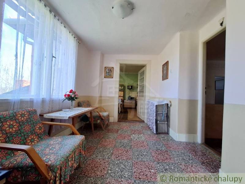 Innenraum eines Einfamilienhauses mit einer Sitzgelegenheit mit Blumenmuster und großen Fenstern, die Licht hereinlassen.