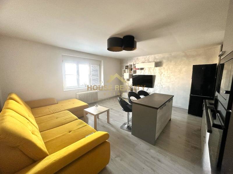 Wohnzimmer mit großem gelbem Sofa, Kücheninsel und Fernseher in einer 2-Zimmer-Wohnung.