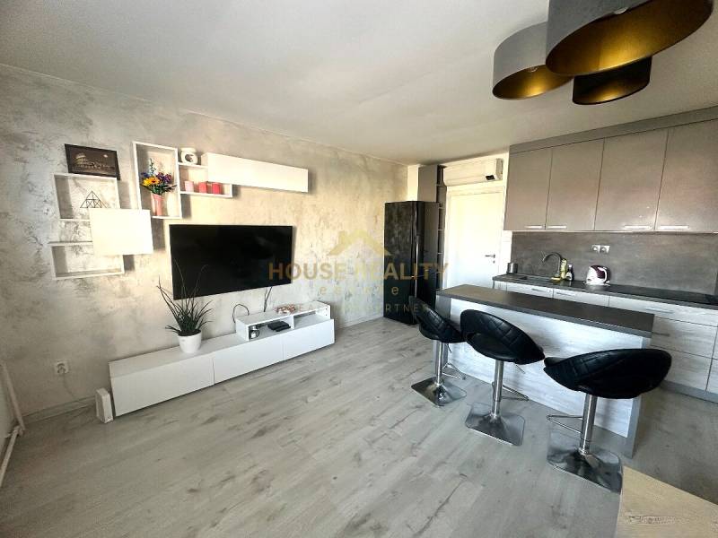 Küche in einer 2-Zimmer-Wohnung mit Fernseher, Holzboden und Bartresen.