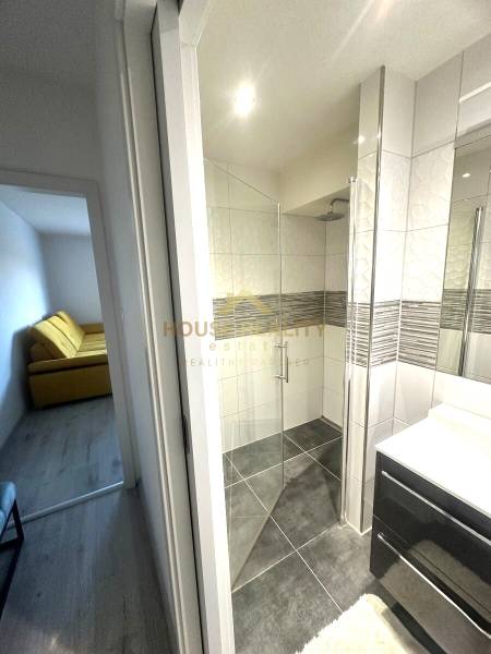 Badezimmer in einer 2-Zimmer-Wohnung mit verglaster Duschkabine und großen Fliesen.
