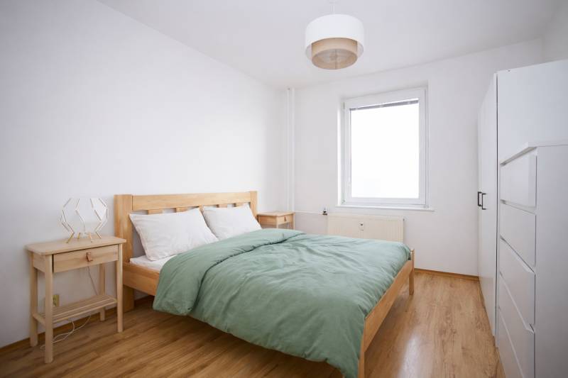 Schlafzimmer in einer 3-Zimmer-Wohnung mit Bett, Nachttischen und Boden mit Holzdekor.