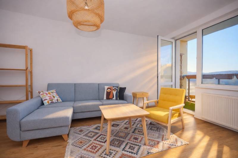 Wohnzimmer mit Sofa, gelbem Sessel, Teppich und Boden mit Holzdekor in einer 3-Zimmer-Wohnung.