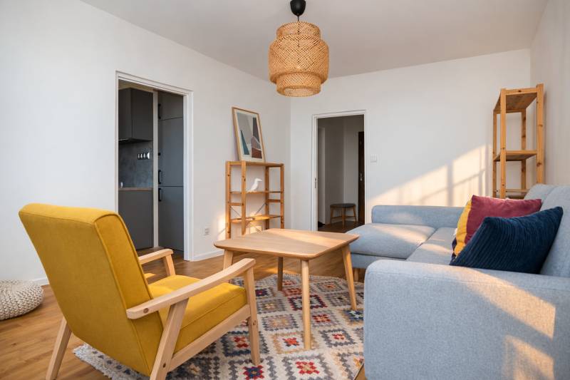 Wohnzimmer in einer 3-Zimmer-Wohnung mit Holzelementen, grauem Sofa und gelbem Sessel.