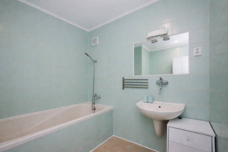 Badezimmer in einer 3-Zimmer-Wohnung mit Badewanne, Waschbecken, Spiegel und hellblauen Fliesen.