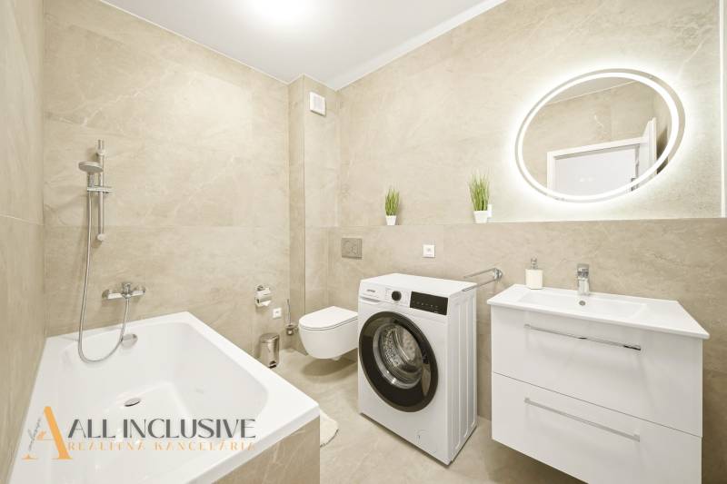 Badezimmer mit Dusche, Waschmaschine und Waschbecken in einer 4-Zimmer-Wohnung mit beigen Fliesen.