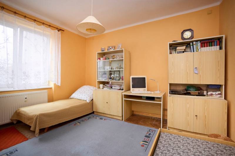 Ein Zimmer in einer 3-Zimmer-Wohnung mit einem Bett, Schränken, einem alten Computer und einer eingeschalteten Lampe.