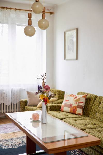 Helles Wohnzimmer in einer 3-Zimmer-Wohnung mit Sofa, Tisch und dekorativen Blumen in einer Vase.