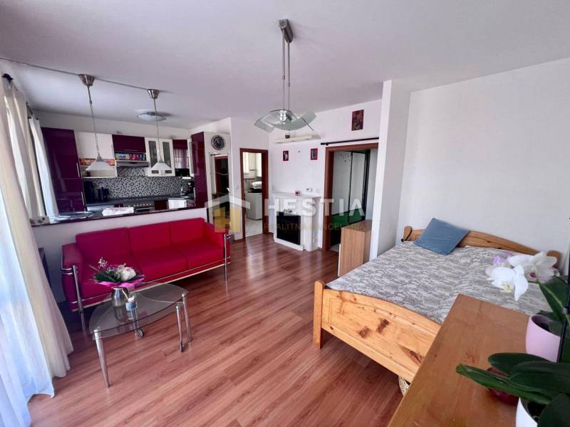 Wohnzimmer mit rotem Sofa, Glastisch und Küche in einer Einzimmerwohnung.
