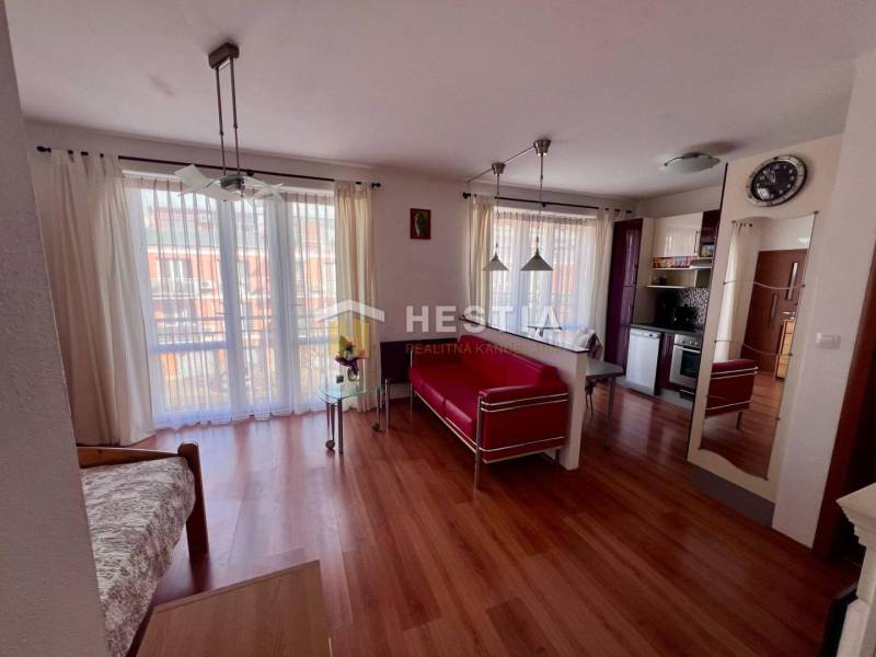 Innenraum einer 1-Zimmer-Wohnung mit Holzboden, Küche, hellen Vorhängen und bequemen Sitzgelegenheiten.