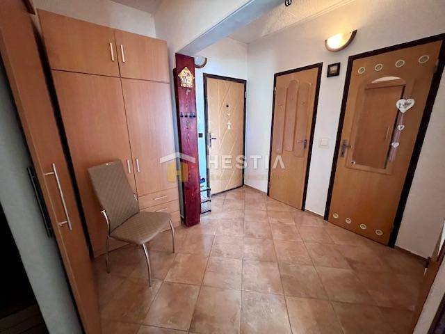 Flur in einer 2-Zimmer-Wohnung mit Fliesen, einem Kleiderschrank und einem Stuhl.