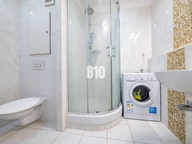 Badezimmer in einer Einzimmerwohnung mit Waschmaschine, Duschkabine und Keramikfliesen.