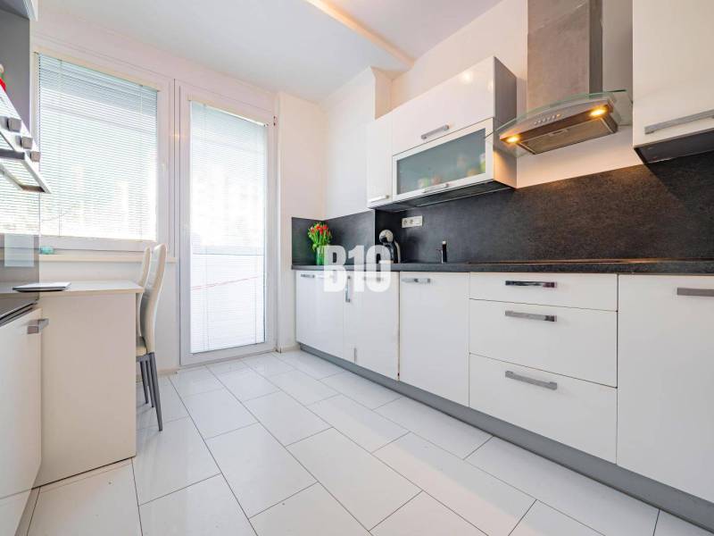 Küche in einer Einzimmerwohnung mit weißen Schränken und dunkler Arbeitsplatte.