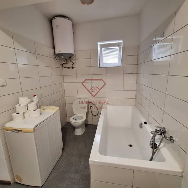 Badezimmer in einem Einfamilienhaus mit Badewanne, Waschmaschine, Boiler und Toilette.