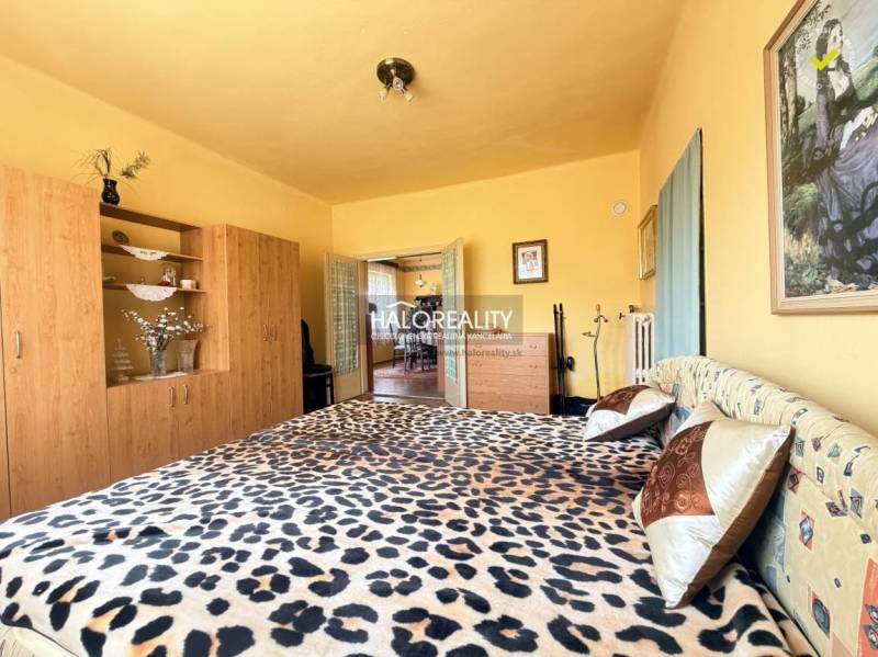 Ein Schlafzimmer in einem Einfamilienhaus mit einem Bett im Leopardenmuster und einem Schrank in Holzoptik.