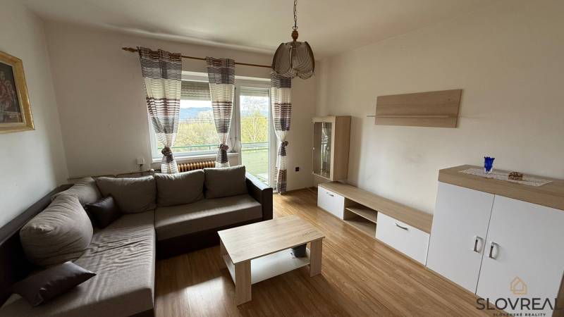 Wohnzimmer in einer 3-Zimmer-Wohnung mit einem bequemen Sofa, einem Boden in Holzoptik und einem Balkon.