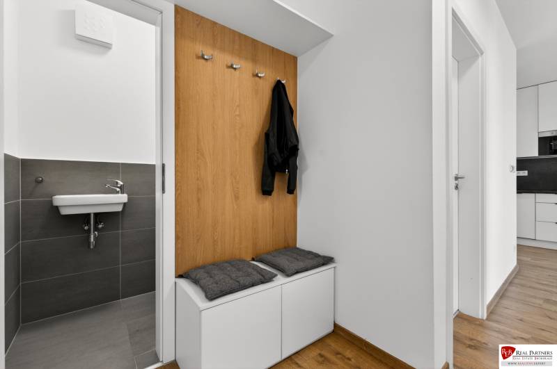 Diele in einer 2-Zimmer-Wohnung mit einer Bank, Kleiderhaken und einem Waschbecken, Boden mit Holzdekor.
