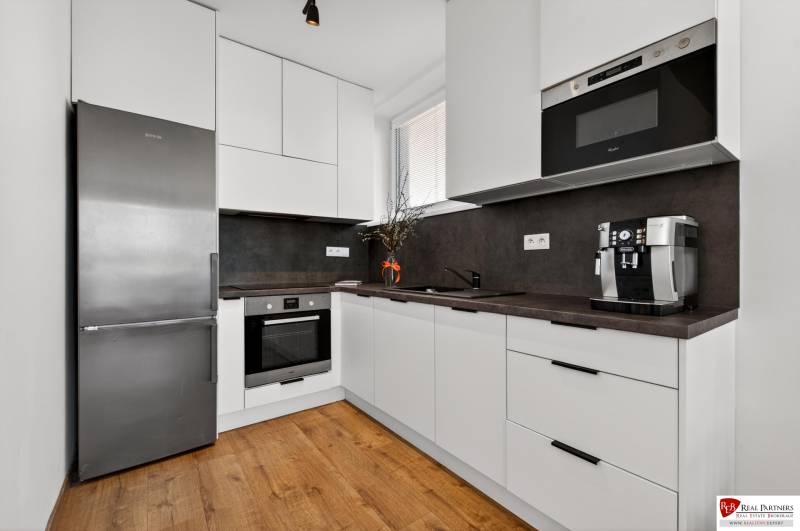 Küche in einer 2-Zimmer-Wohnung mit Holzboden, weißen Schränken, Geräten.
