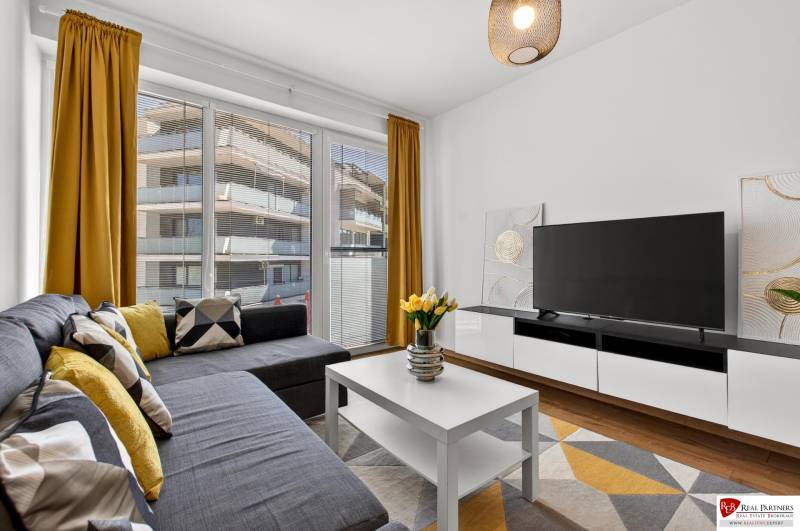 Zweizimmerwohnung mit großen Fenstern, Sofa, Fernseher, gelben Vorhängen und Holzboden.