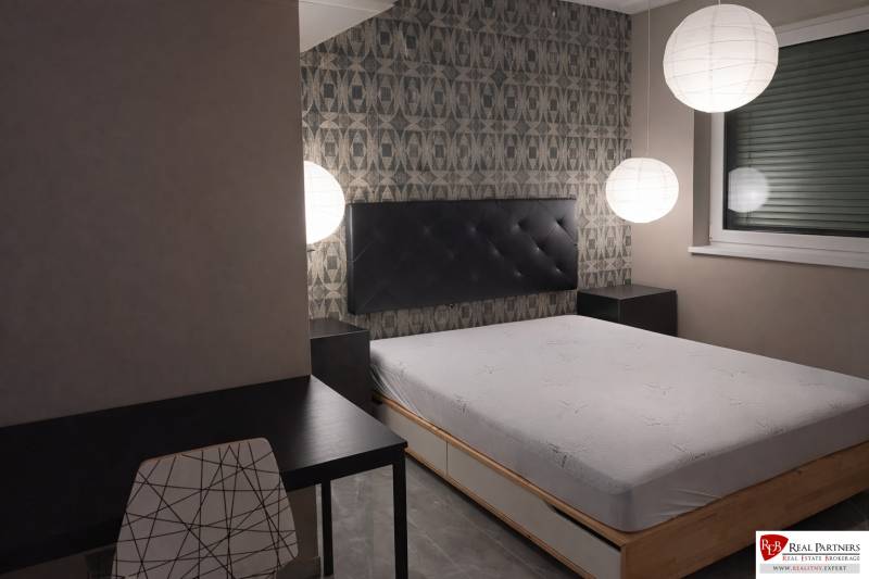 Schlafzimmer mit Bett, Abendbeleuchtung, Tisch und Stuhl in einer Zweizimmerwohnung.
