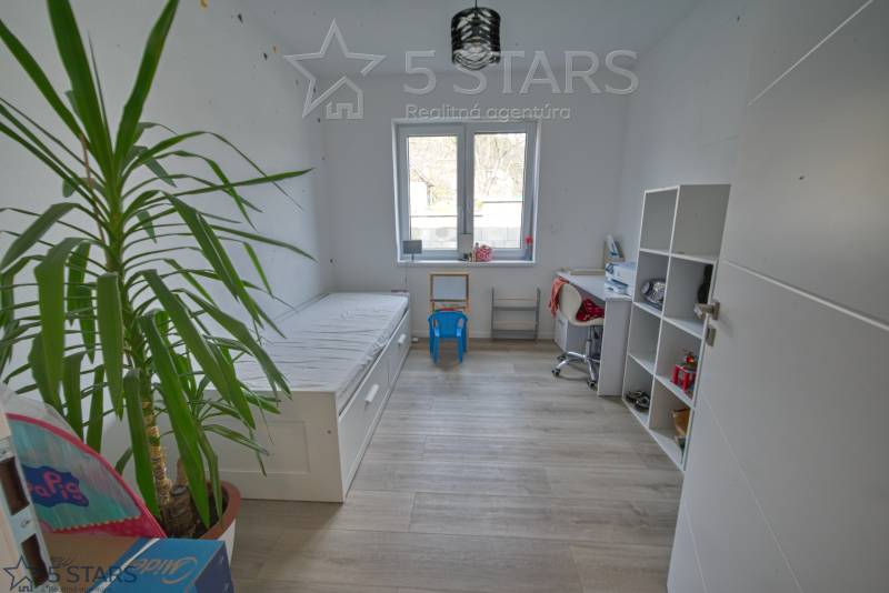 Kinderzimmer in einem Einfamilienhaus mit Bett, Tisch und Regal auf einem Boden mit Holzdekor.