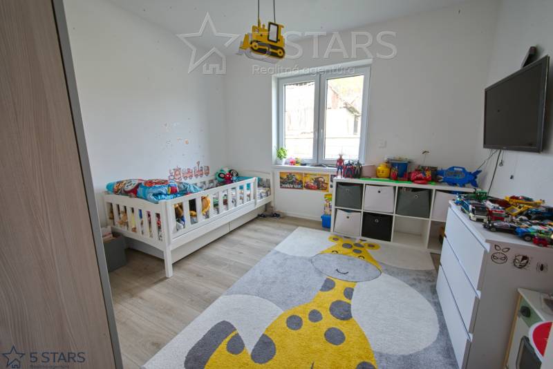 Kinderzimmer mit Bett, Spielzeug, Teppich mit Giraffenmotiv, Boden mit Holzdekor.