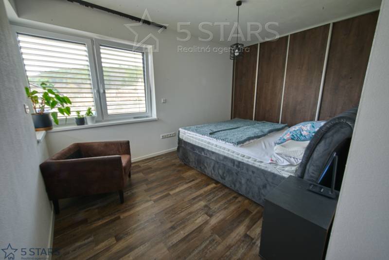Schlafzimmer in einem Einfamilienhaus mit Bett, Sessel und Boden in Holzoptik.