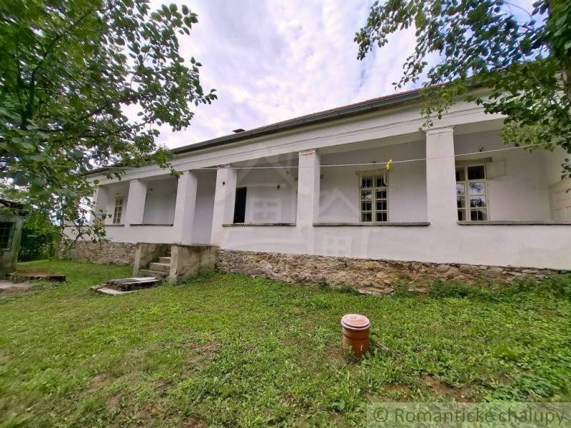 Ein Einfamilienhaus in Dobroč, weiße Fassade, steinerne Basis, umgeben von Grün und Bäumen.