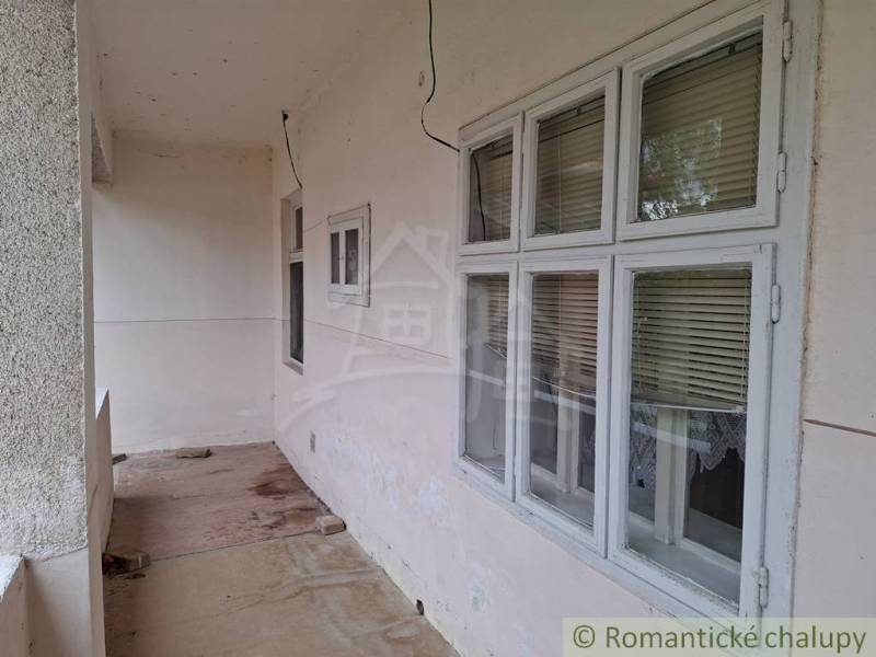 Ein Einfamilienhaus in Mužla mit einer durchgehenden Terrasse, Fenstern mit Jalousien und einem Betonboden.