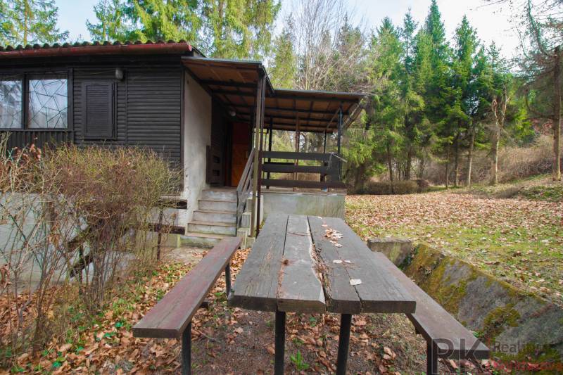 Eine Hütte mit Terrasse und Tisch auf den Erholungsgrundstücken in Holčíkovce, umgeben von Wald.