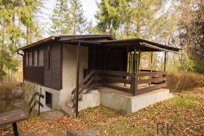 Eine Holzhütte auf Erholungsgrundstücken in Holčíkovce, umgeben von Bäumen und gefallenem Laub.