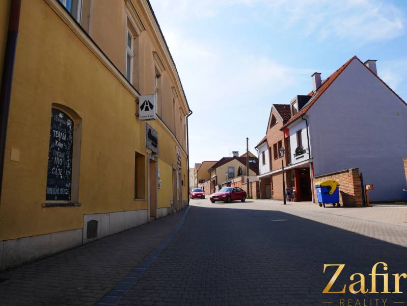 Eine Straße in Trnava mit Gastronomiebetrieben, gelbe und Backsteingebäude, geparktes Auto.