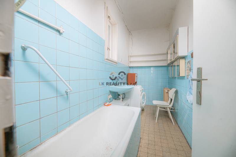 Badezimmer mit blauen Fliesen, Waschbecken, Badewanne, Waschmaschine und Regalen im Einfamilienhaus.
